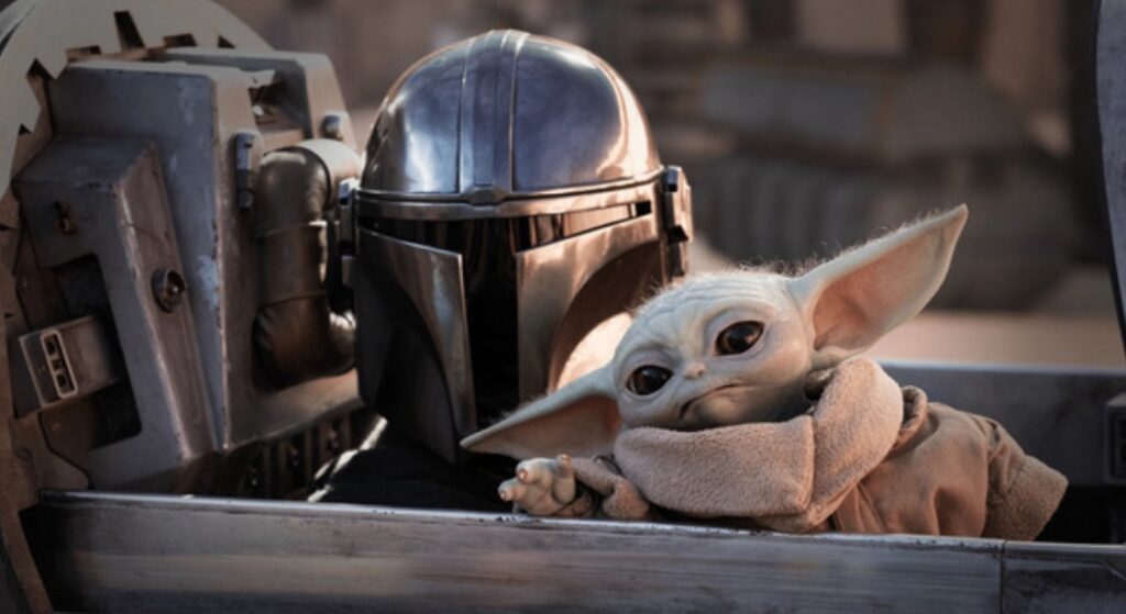 A close-up still from The Mandalorian featuring Din Djarin and Grogu sitting together in the cockpit of the N-1 Starfighter. The Mandalorian’s beskar helmet is visible in the background, while Grogu leans forward in the foreground.