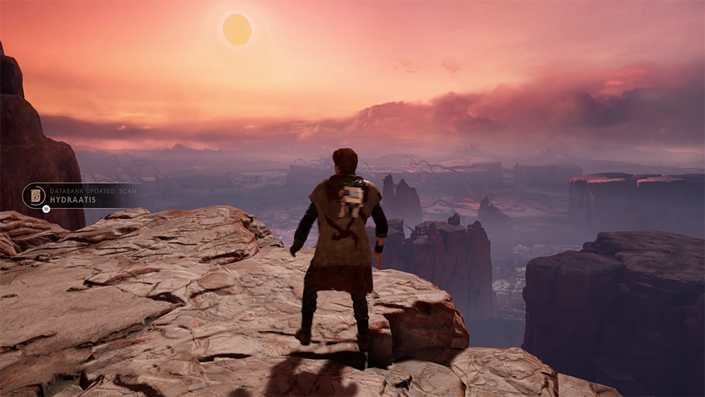 Cal Kestis stands on a rocky cliff ledge from behind with BD-1 on his back, overlooking a vast, misty canyon landscape under a warm sunset sky of Dathomir in Star Wars Jedi: Fallen Order.